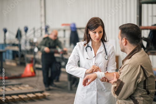 Doctor bandaging arm of a injured factory worker.