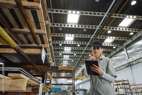 Portrait of a female warehouse worker in large warehouse looking at clipboard, low angle view.
