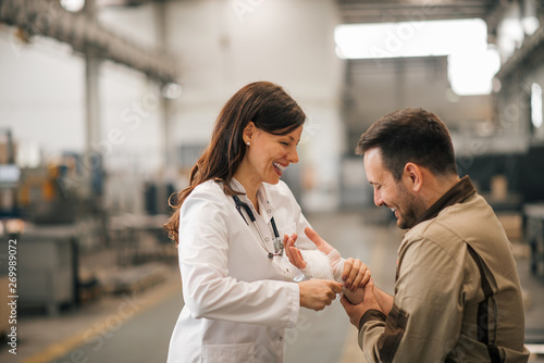 Canvas Print Smiling female doctor with injured worker in the industrial building