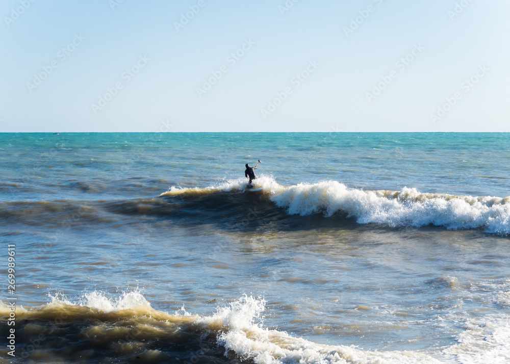 A man in a black wetsuit on the surf of the Black Sea Sochi 05.12.2019