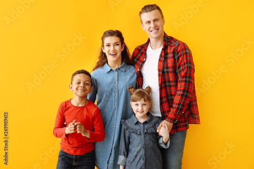 Happy couple with little adopted children on color background