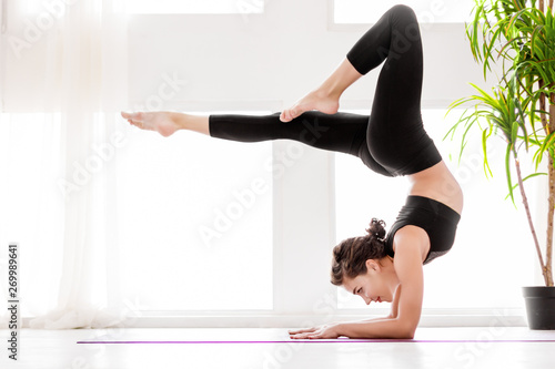 Young healthy fitness beautiful woman female doing vrischikasana yoga posture and yoga workout on yoga mat at yoga studio in morning. Healthy lifestyle, morning workout concept