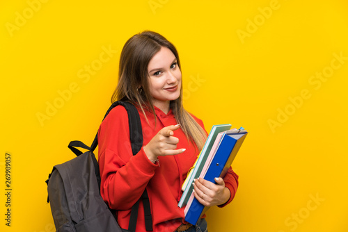 Teenager student girl over yellow background points finger at you