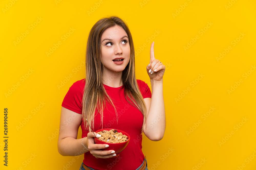 Young teenager girl holding a bowl of cereals intending to realizes the solution while lifting a finger up Young teenager girl holding a bowl of cereals intending to realizes the solution while lifting a finger up