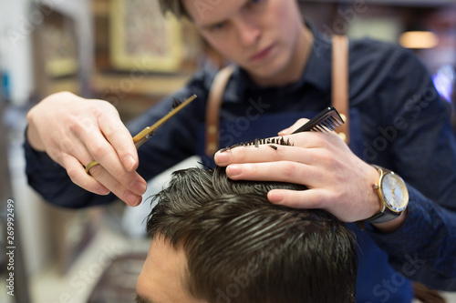 grooming, hairdressing and people concept - close up of male client and hairdresser with comb and scissors cutting hair at barbershop