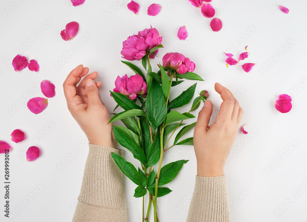 two hands of a young girl with smooth skin and a bouquet of red peonies