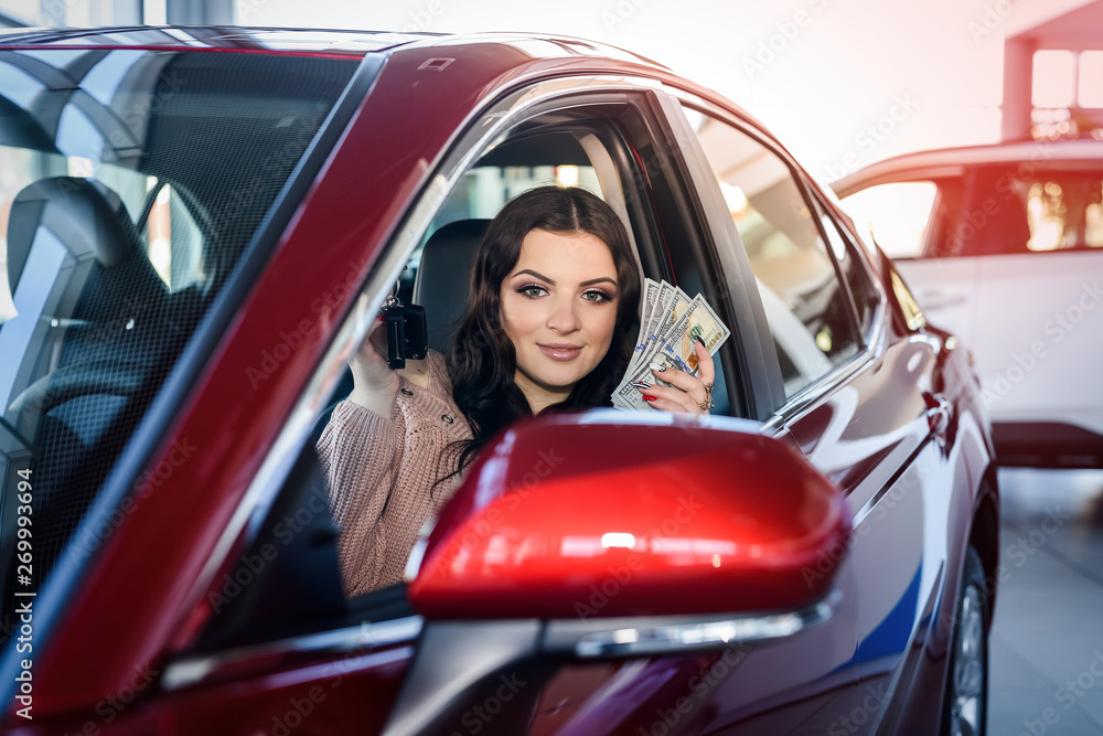 Woman sitting in new car and showing dollars and keys