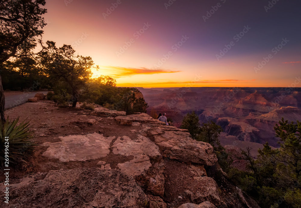 couple sitting on the edge of a precipice, observing the bucolic and relaxing landscape during the sunset, of the great canyon of colorado, in arizona