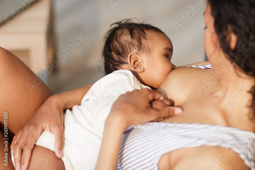 Close-up of young black mother attaching baby at breast while giving nipple to son during breastfeeding photo