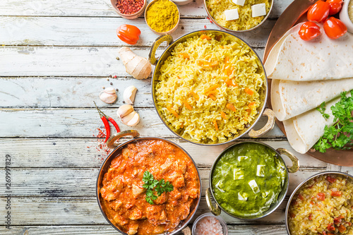 Different bowls with assorted indian food on white wooden background, top view. Dishes and appetizers of indian cuisine. Chicken, curry rice, lentils, paneer, chapati and spices.