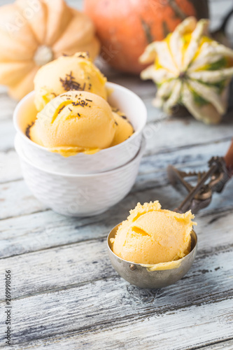 Scoop of gourmet pumpkin ice cream, gelato in white bowl over wooden background