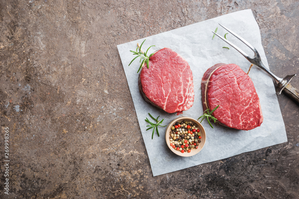 Raw marbled meat steak Filet Mignon with seasonings over stone background, top view. Raw marbled meat steak Filet Mignon with seasonings over stone background, top view.