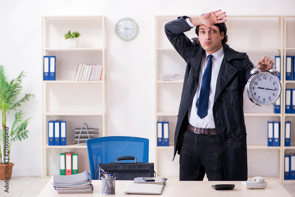 Young male employee in the office in time management concept Young male employee in the office in time management concept