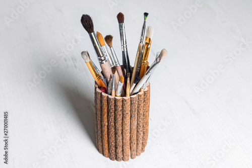 Painter brushes in wooden cup on white table 