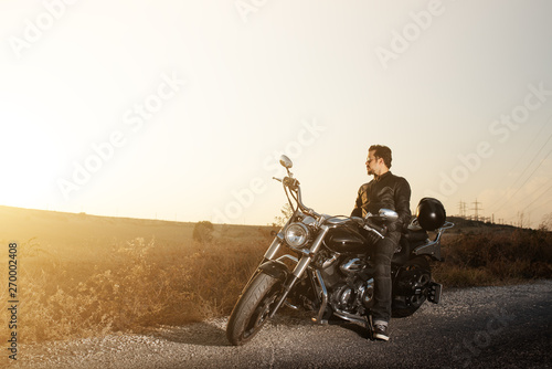 Side view of a young male biker sitting on the side of the road against sunset while traveling by bike.