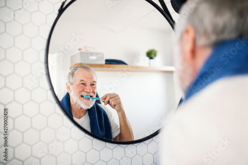 A senior man brushing teeth in bathroom indoors at home. Copy space. photo