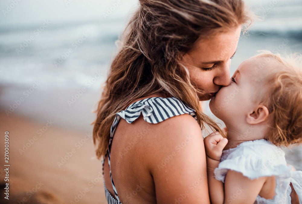 Close-up of young mother with a toddler girl on beach on summer holiday, kissing. Close-up of young mother with a toddler girl on beach on summer holiday, kissing.