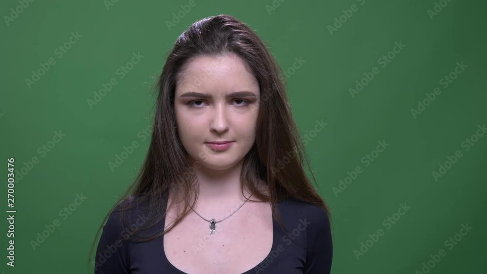 Closeup portrait of young pretty brunette female tossing her hair and looking at camera with confusion with background isolated on green Closeup portrait of young pretty brunette female tossing her hair and looking at camera with confusion with background isolated on green
