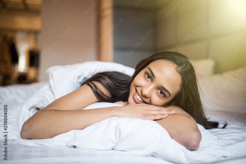 Young woman looking at camera and smiling while lying on the bed at home Young woman looking at camera and smiling while lying on the bed at home
