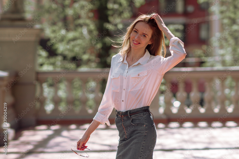 Beautiful girl with long hair in a white blouse smiling against a background of trees and a beautiful fence Beautiful girl with long hair in a white blouse smiling against a background of trees and a beautiful fence