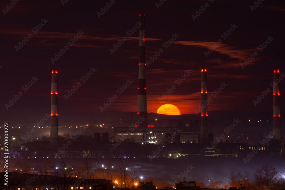 Beautiful moonrise on the background of factory pipes and the city of Novokuznetsk in Russia