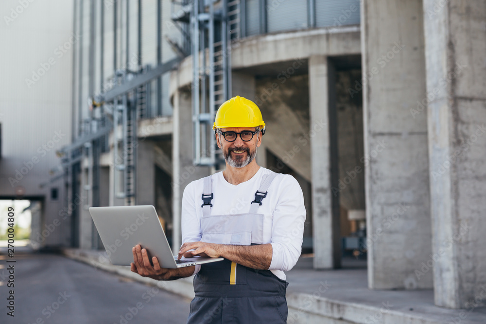 worker using laptop standing in front of grain silo worker using laptop standing in front of grain silo