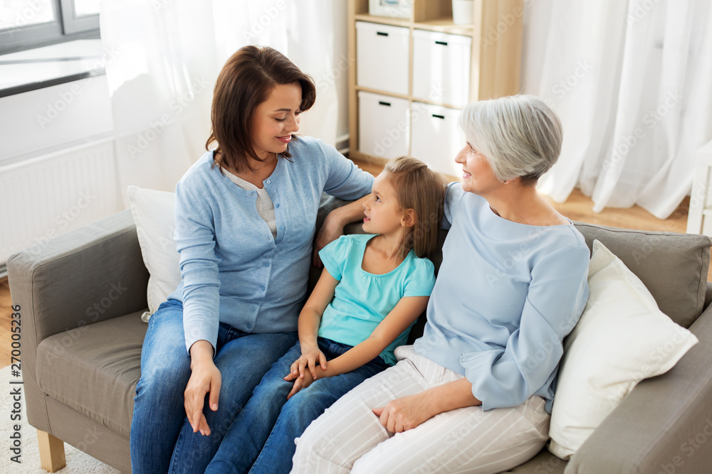 family, generation and female concept - portrait of smiling mother, daughter and grandmother sitting on sofa at home