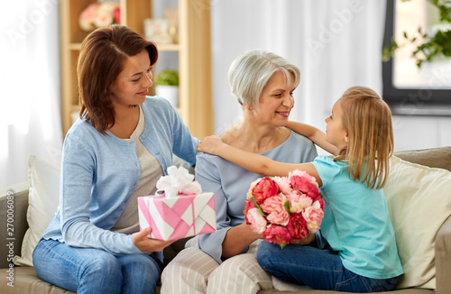 family, generation and birthday - happy mother with gift box and daughter hugging grandmother at home