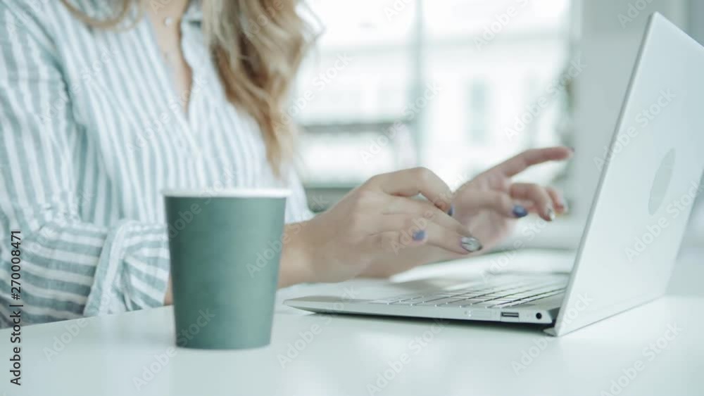 Closeup panning shot of unrecognizable female entrepreneur sitting at desk and typing on laptop computer, paper cup of coffee nearby Closeup panning shot of unrecognizable female entrepreneur sitting at desk and typing on laptop computer, paper cup of coffee nearby