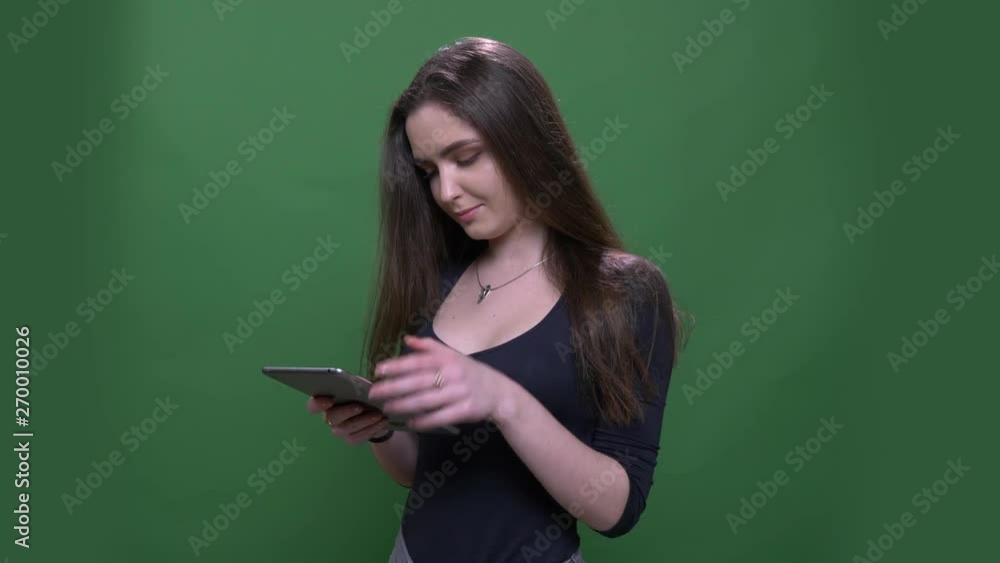 Closeup portrait of young pretty brunette female using the tablet and smiling happily with background isolated on green Closeup portrait of young pretty brunette female using the tablet and smiling happily with background isolated on green