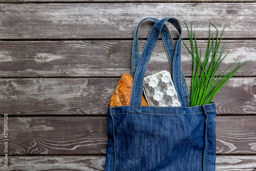 Fresh produce in blue denim market bag on wooden background, flat lay. Eco friendly reusable shopping bag for minimize waste, Earth Day, no plastic.