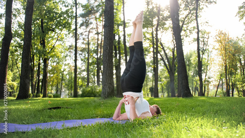 Image of mid aged smiling happy woman meditating and doing yoga exercises on grass at forest. Woman taking care of her physical and mental health while pracitising fitness and stretching at park photo