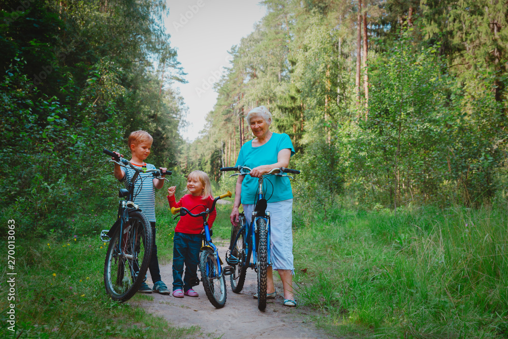 Naklejka premium active senior grandmother with kids riding bikes in nature