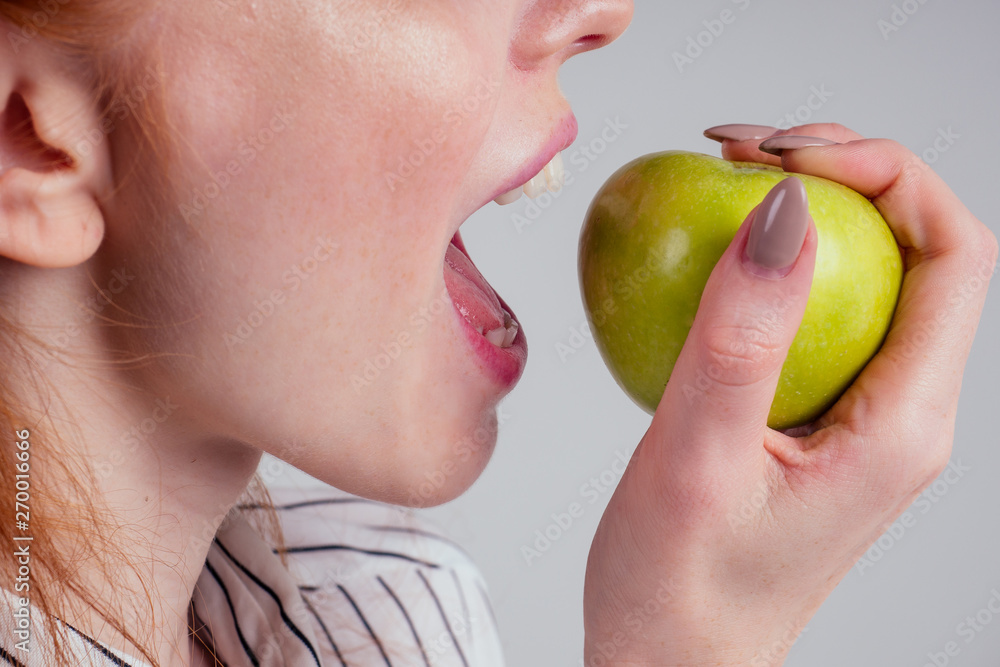 beautiful young redhead businesswoman in a striped shirt snow-white smile and perfect skin eating detox green apple in studio white background(healthy snack student) beautiful young redhead businesswoman in a striped shirt snow-white smile and perfect skin eating detox green apple in studio white background(healthy snack student)