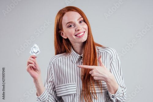 picture of young redhead be lost in thought businesswoman in striped shirt with pack of condom and birth choosing thinking white background studio photo