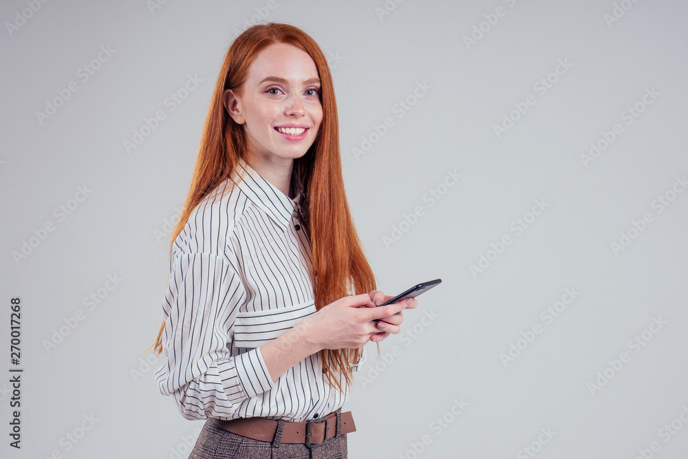 Cheerful redheared woman businesswomen in a striped shirt showing blank smartphone screen white background studio Cheerful redheared woman businesswomen in a striped shirt showing blank smartphone screen white background studio
