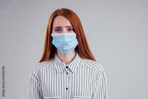 unhappy redhead woman green eyes businesswomen in a striped shirt wearing gauze blue mask white background studio