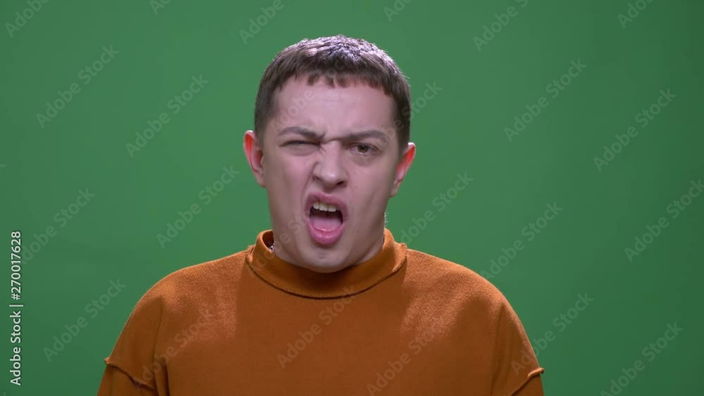 Closeup shoot of young attractive caucasian male showing tongue making funny facial expressions looking at camera with background isolated on green Closeup shoot of young attractive caucasian male showing tongue making funny facial expressions looking at camera with background isolated on green