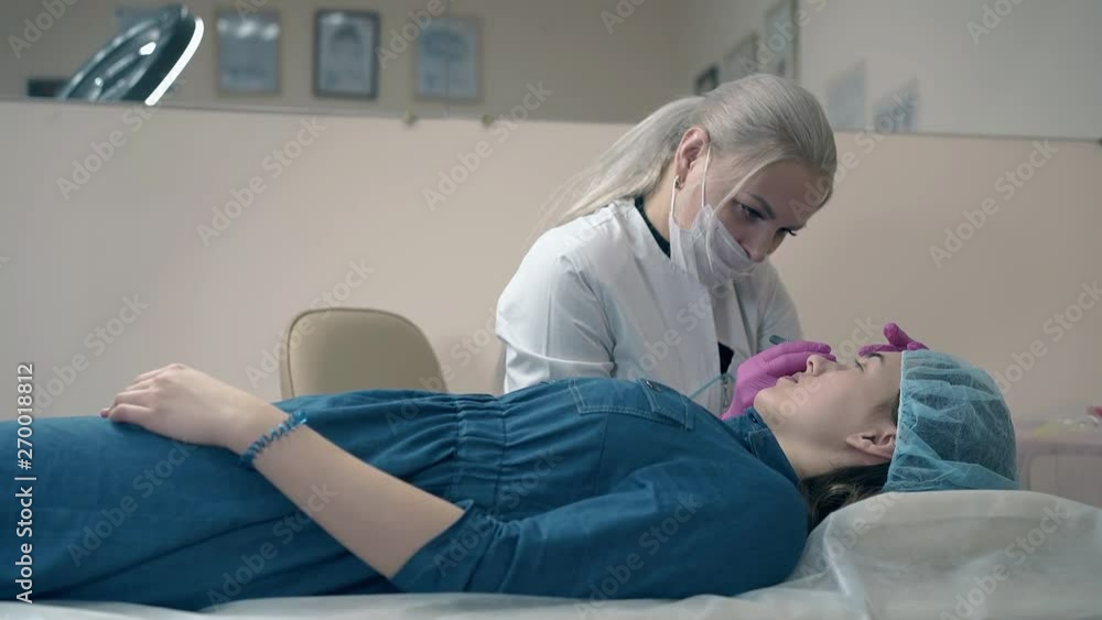 woman in mask and coat uses tweezer to work with client brows in cosmetology salon slow motion woman in mask and coat uses tweezer to work with client brows in cosmetology salon slow motion