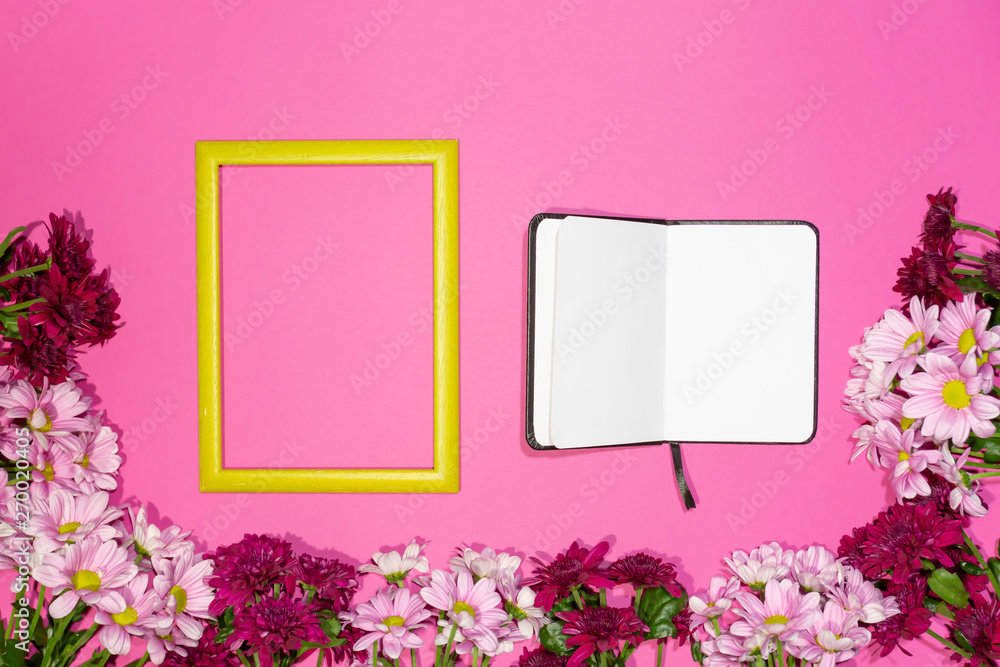 Design concept - top view of blank notebook page and spring flowers isolated on black background with yellow frame for mockup