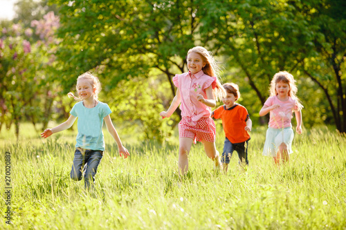 a group of children playing and running in the park on a green gozon.