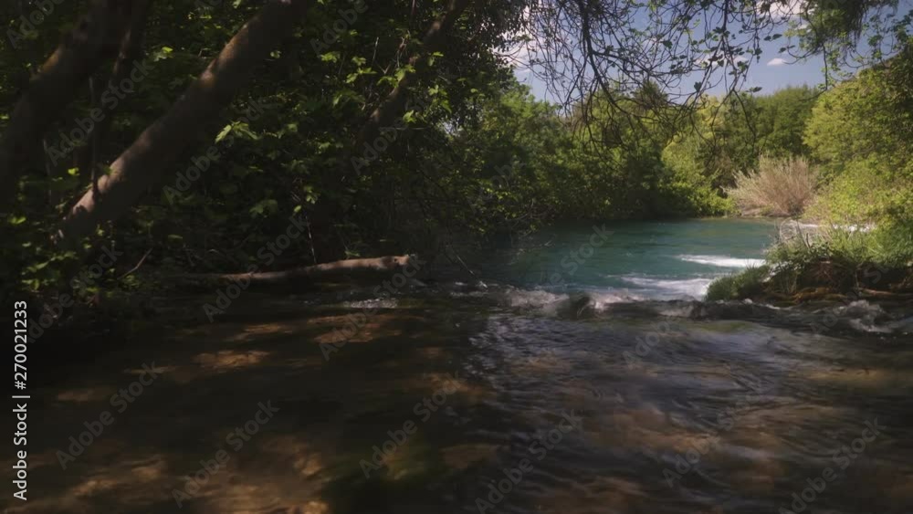 Dolly shot under shaded trees moving over fast flowing river water into cal tranquil turquoise lake at Krka national park, Croatia. Dolly shot under shaded trees moving over fast flowing river water into cal tranquil turquoise lake at Krka national park, Croatia.