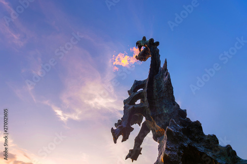 Symbol of Cracow - legendary polish wawel dragon monument with fire coming out from its mouth against blue sky at sunset.