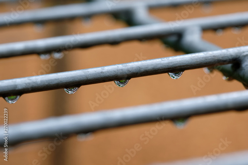 Raindrops hanging on a gray iron grid of a soccer goal on a playground with a brown background