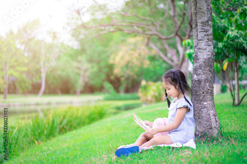 Cute little girl reading a book with a doll in the park