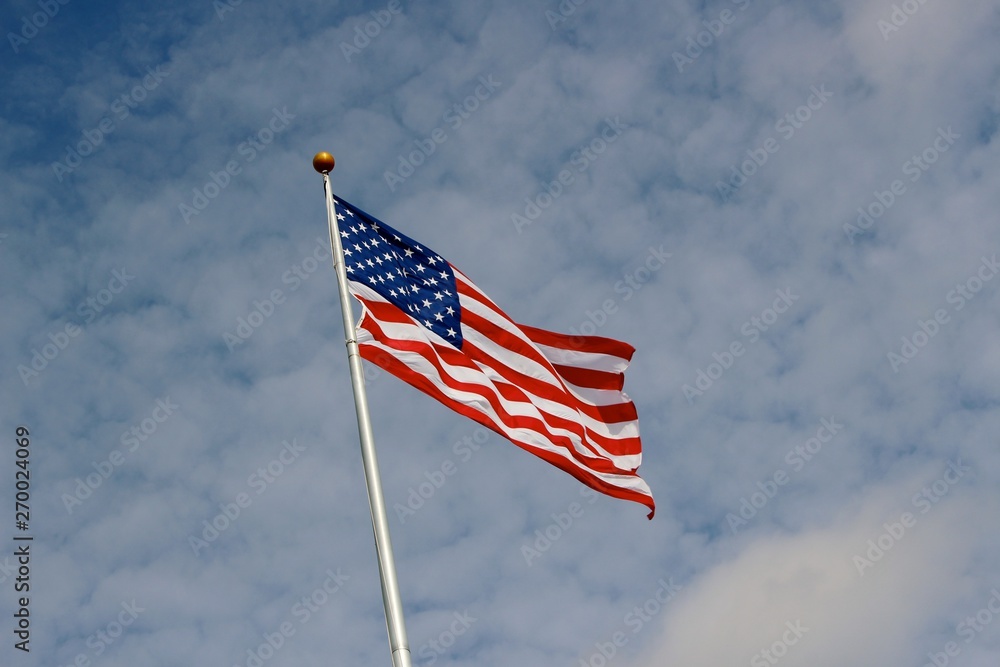 American flag flying in the breeze with a puffy blue cloud sky. American flag flying in the breeze with a puffy blue cloud sky.