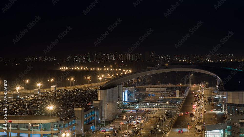Night shot of intense car traffic on the road with overpass and full multilevel parking lot