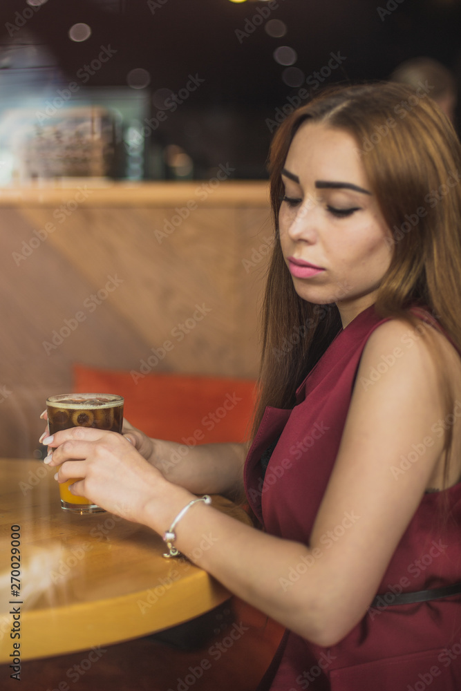 Φωτογραφία beautiful girl holds a glass of cold coffee mixed with ice and orange juice on cafe background