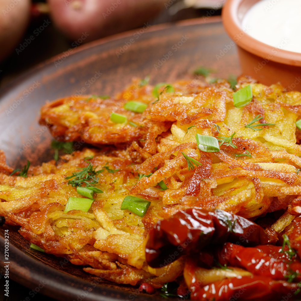Closeup view at Homemade tasty potato pancakes in clay dish with sun-dried tomatoes and sour creram Closeup view at Homemade tasty potato pancakes in clay dish with sun-dried tomatoes and sour creram