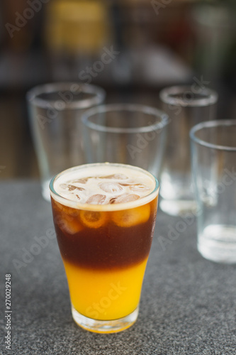 cold brew coffee with orange juice. Glass with cold coffee and ice on the background of a bag and chaotically scattered coffee beans and orange. Selective focus